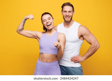 Young strong fitness trainer sporty two man woman wear blue clothes spend time in home gym show hand biceps muscles point camera on you isolated on plain yellow background. Workout sport fit concept - Powered by Shutterstock