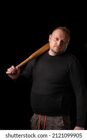 A Young Strong Man Holds A Bat In His Hand. Dark Background. A Large Man In Black Clothes. Bouncer, Security Guard, Bodyguard Concept.