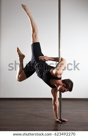 Young strong pole dancer man in black clothes on pylon. Neutral background