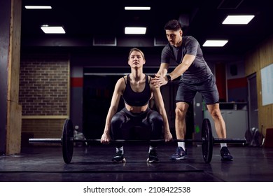 A young strong sportswoman lifting weights in gym with her personal trainer. - Shutterstock ID 2108422538
