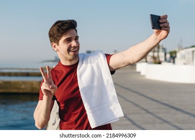 Young Strong Sporty Athletic Fit Sportsman Man In Sports Clothes Do Selfie Shot On Mobile Cell Phone Show V-sign Warm Up Training At Sunrise Sun Dawn Over Sea Beach Outdoor On Pier Seaside In Morning