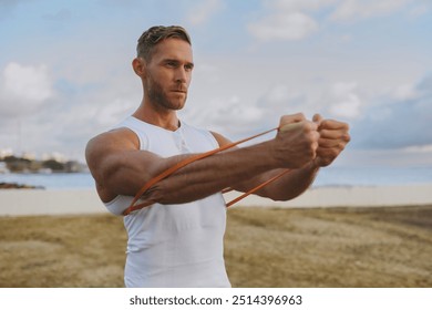 Young strong sporty athletic fit sportsman man wearing sports clothes using elastic rubber band for hands warm up training at sunrise sun dawn over sea beach outdoor on seaside in summer day morning - Powered by Shutterstock