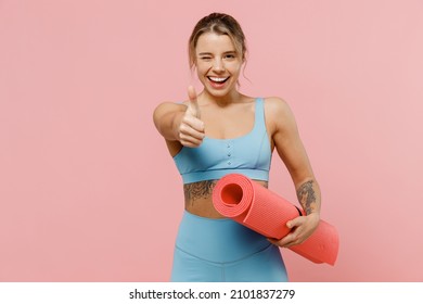 Young strong sporty athletic fitness trainer instructor woman wear blue tracksuit spend time in home gym show thumb up gesture blink isolated on pastel plain pink background. Workout sport concept. - Shutterstock ID 2101837279