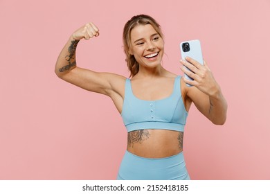 Young strong sporty athletic fitness trainer woman wear blue tracksuit spend time in home gym do selfie shot on mobile cell phone show muscles isolated on plain pink background. Workout sport concept - Powered by Shutterstock