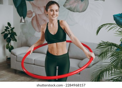 Young strong sporty athletic fitness trainer instructor woman wearing green tracksuit hold using hula hoop for slim waist training do exercises at home gym indoor. Workout sport motivation concept - Powered by Shutterstock