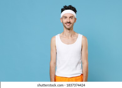 Young Strong Sporty Fitness Man With Thin Skinny Body Sportsman In White Headband Shirt Shorts Doing Stretching Exercising For Hands Isolated On Blue Background. Workout Gym Sport Motivation Concept