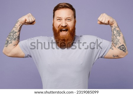 Young strong sporty fitness redhead bearded man he wear violet t-shirt casual clothes show biceps muscles on hand demonstrating strength power isolated on plain pastel light purple background studio