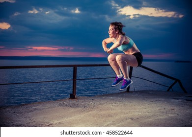 Young Strong Woman In Sportswear Doing Plyometric Exercises On Pier. Jump Squats, Fitness Workout Outdoors.