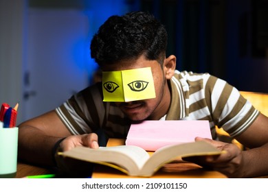 Young student acting like reading while sleeping by putting eye open stickers at home - concept of lazyiness and late night studying, careless and negligence.