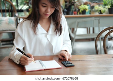 Young Student Asia Woman Holding Pen For Writing On Notebook Paper And Using Calculator For Calculate. Image For Business,education,people And Portrait Concept