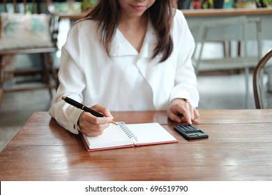 Young Student Asia Woman Holding Pen For Writing On Notebook Paper And Using Calculator For Calculate. Image For Business,education,people And Portrait Concept