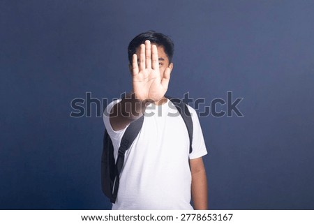 Young student with a backpack making a stop gesture with his hand covering his face.