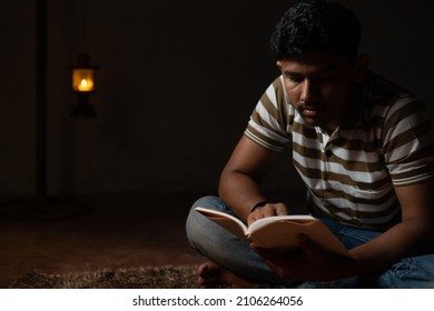 Young Student Busy Reading During Night Under Oil Lamp Or Lantern Due To Power Loss And Poverty - Concpet Of Power Cut, Blackout During Examination.