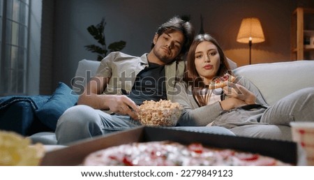 Young student caucasia n couple spending time together on couch, sitting in front of tv, watching random shows in absolute boredom, tired after a long day eating unhealthy food 4k footage Foto stock © 