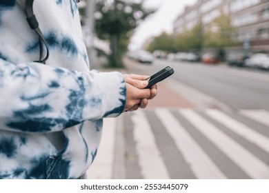 Young student checking their phone while standing outdoors in a city setting - Powered by Shutterstock