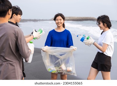 Young student collecting plastic waste on the beach. People cleaning the beach up - Powered by Shutterstock