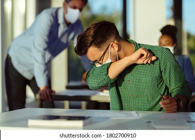 Young student coughing into elbow while wearing protective face mask at lecture hall.  - Powered by Shutterstock