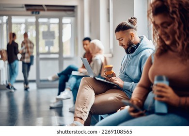 Young student drinking coffee while using laptop in hallway at the university. - Powered by Shutterstock