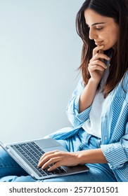 Young student e-learning on laptop at home, cute small dog besides. Businesswoman working remotely, sitting on bed. Homeoffice for single woman living alone. People and technology issues