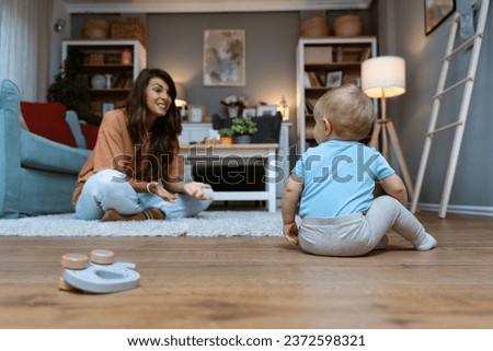 Young student girl babysitter playing with baby on the floor of apartment working to pay her scholarship, taking care of child while parents are on their work or date night.