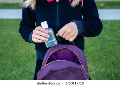 Young student girl holding hand sanitizer bottle putting to her school purple backpack. Ready for new school year with pandemic restrictions. School reopening. Return back to school, new life concept. - Powered by Shutterstock