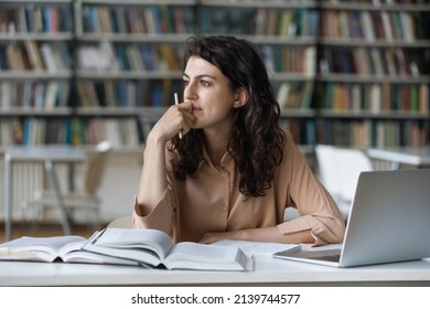 Young student girl sit at table with textbooks and laptop staring aside, studying alone in library, looks pensive and thoughtful search solution, prepare for exam, makes task feels confused or puzzled - Shutterstock ID 2139744577