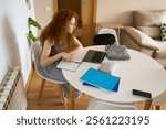 Young student girl studying at home using laptop and taking notes