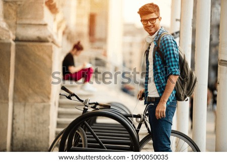 young student with glasses parking his bicyle on bicyle place in front university