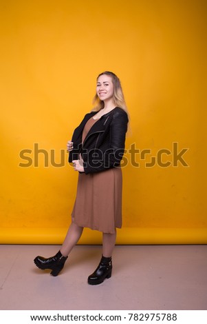 young student with long blonde hair posing in Studio. emotional portrait. street style: spring dress and a light jacket. clean face and long legs. cheerful woman dancing on a colored background