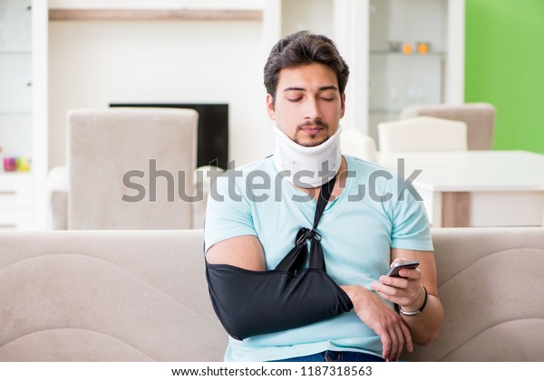 Young student man with neck and hand injury sitting\
on the sofa