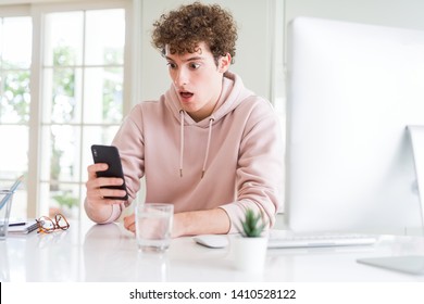 Young Student Man Using Smartphone And Computer Scared In Shock With A Surprise Face, Afraid And Excited With Fear Expression