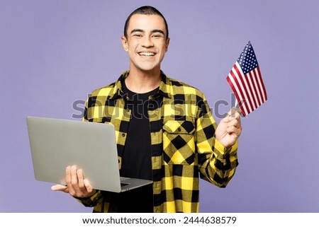 Young student IT middle eastern man wears yellow shirt casual clothes hold American flag use work on laptop pc computer isolated on plain pastel purple background studio portrait. Lifestyle concept