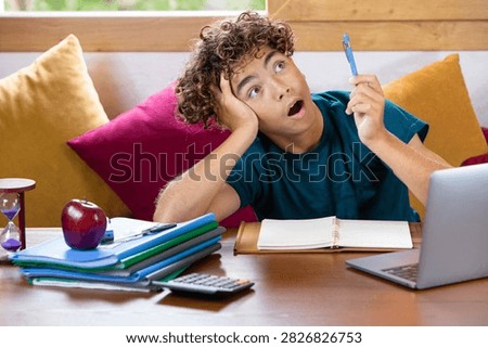 Young student procrastinating while studying at home, looking distracted and overwhelmed by homework, with laptop, notebooks, calculator, apple and hourglass on the desk. Concept of education, stress, time management and lack of focus.