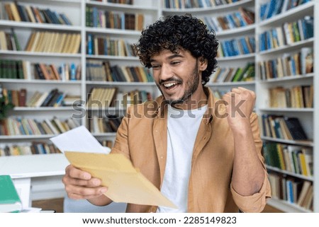 Young student received letter with good exam results and university admission confirmation, hispanic man with curly hair celebrating successful achievement holding hand up close up.