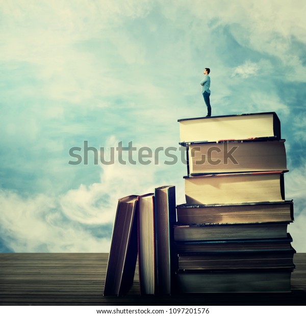 Young student stand on the top of a huge pile of books looking far at horizon. Idea and knowledge concept.