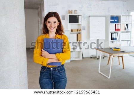 Young student stands in an office with her application documents and laughs into the camera