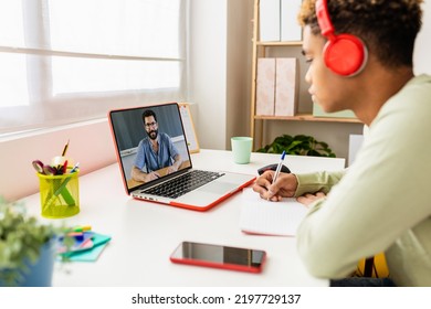 Young student studying from room watching lesson online on laptop. Hispanic latin teenager boy taking notes while listening male teacher on virtual video call. Education and learning distance concept - Powered by Shutterstock