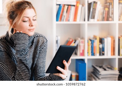 Young student using e-book and bookshelf on background