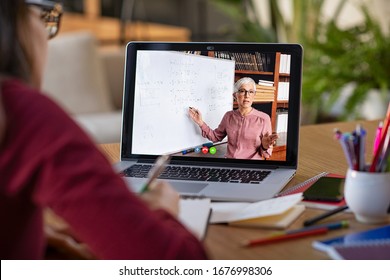 Young student watching lesson online and studying from home. Young woman taking notes while looking at computer screen following professor doing math on video call. Girl studying from home on pc. - Shutterstock ID 1676998306