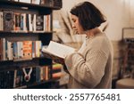 Young student woman drink coffee and browsing bookshelves in a bookstore. Education, school studying, reading concept. Woman are looking a the bookshelves thinking what book to buy at the bookstore.