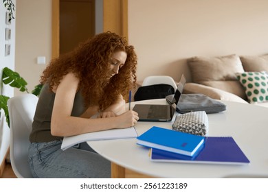 Young student writing notes while studying at home using laptop