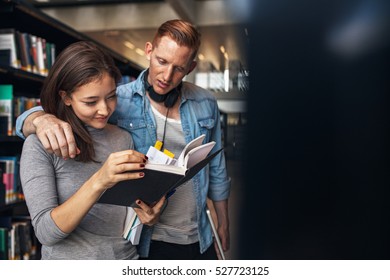 Young students finding reference books in university library. Man and woman university students standing by bookshelf in library and reading a book.