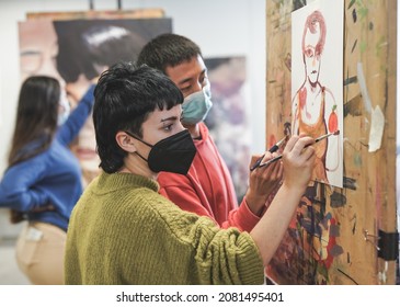 Young students painting together inside art room at school while wearing safety face mask for coronavirus outbreak