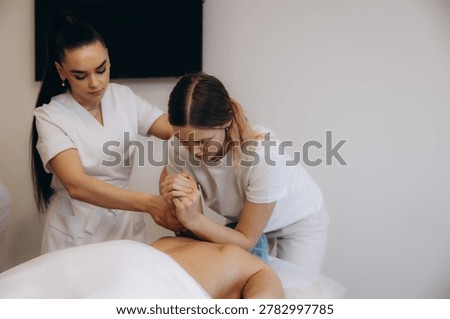 Young students practicing massage techniques on a client's back, receiving instruction during a training session at a spa school