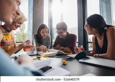 Young Students Sitting At A Table In A Library And Reading Books For Their Class Assignment. University Students Doing Group Study In Library.