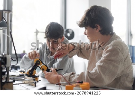 Young students using a 3D printer in the lab at school, one is using a screwdriver