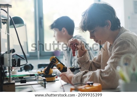 Young students using a 3D printer in the lab at school, one is using a screwdriver
