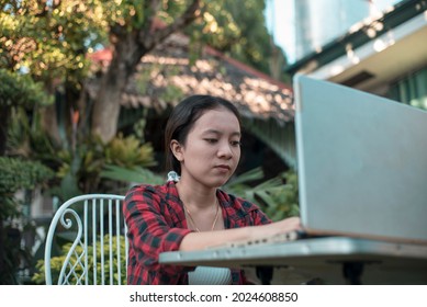 A young studious Filipino woman does her homework on the laptop while sitting out at the garden. Busy and serious mood.