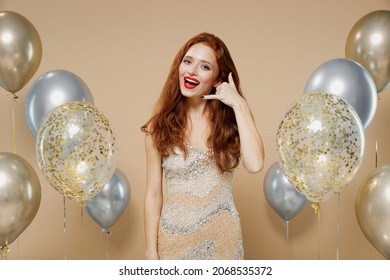 Young stunning redhead woman 20s in evening dress near balloons doing phone gesture like says call me back isolated on plain pastel beige background studio portrait. Celebrating birthday party concept