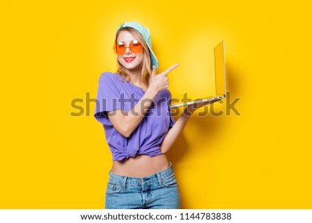 Young style girl with orange glasses and laptop computer on yellow background. Clothes in 1980s style